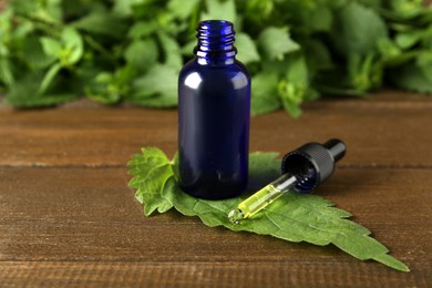 Photo of Glass bottle of nettle oil with dropper and fresh leaf on wooden table
