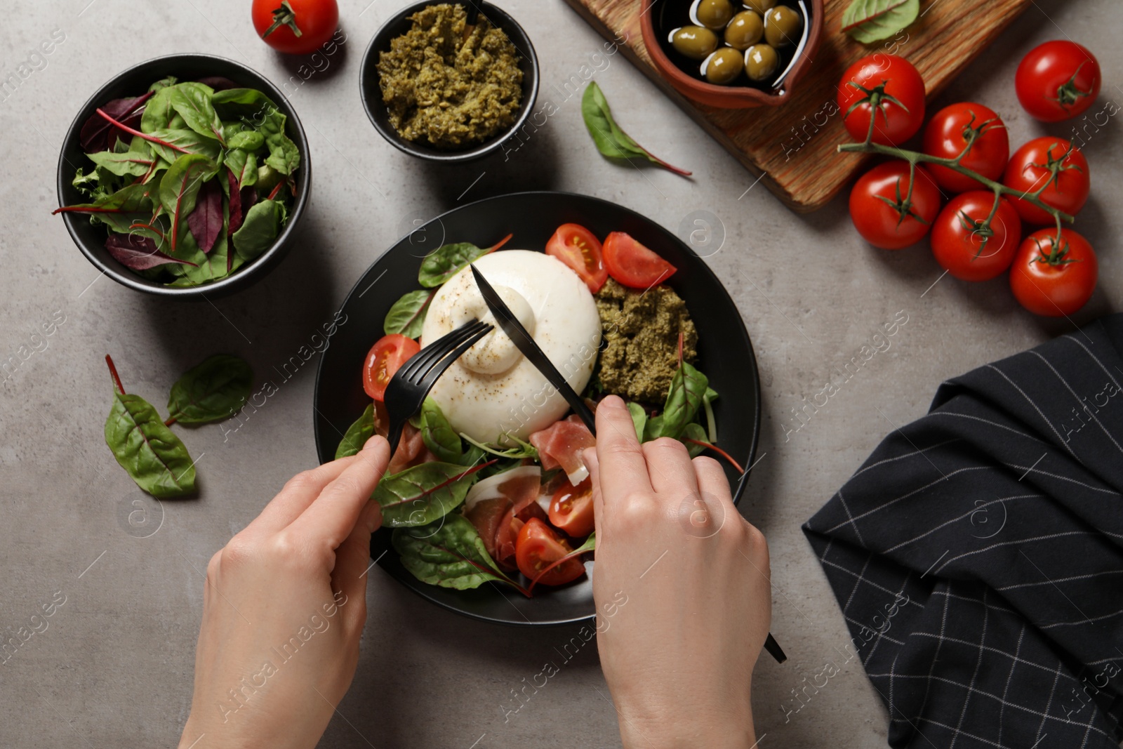 Photo of Woman eating delicious burrata salad at grey table, top view