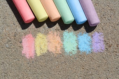 Photo of Colorful chalk sticks and strokes on asphalt outdoors, flat lay