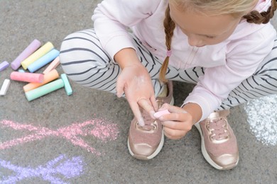 Photo of Little child drawing her hands with chalk outdoors, closeup