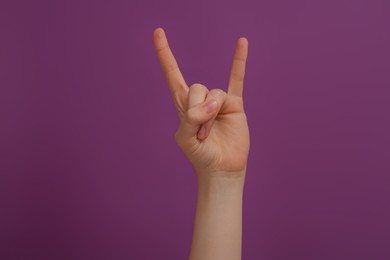Photo of Woman showing gesture of horns on purple background, closeup