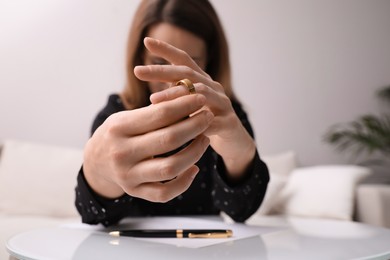 Photo of Woman taking off wedding ring at table indoors, focus on hands. Divorce concept