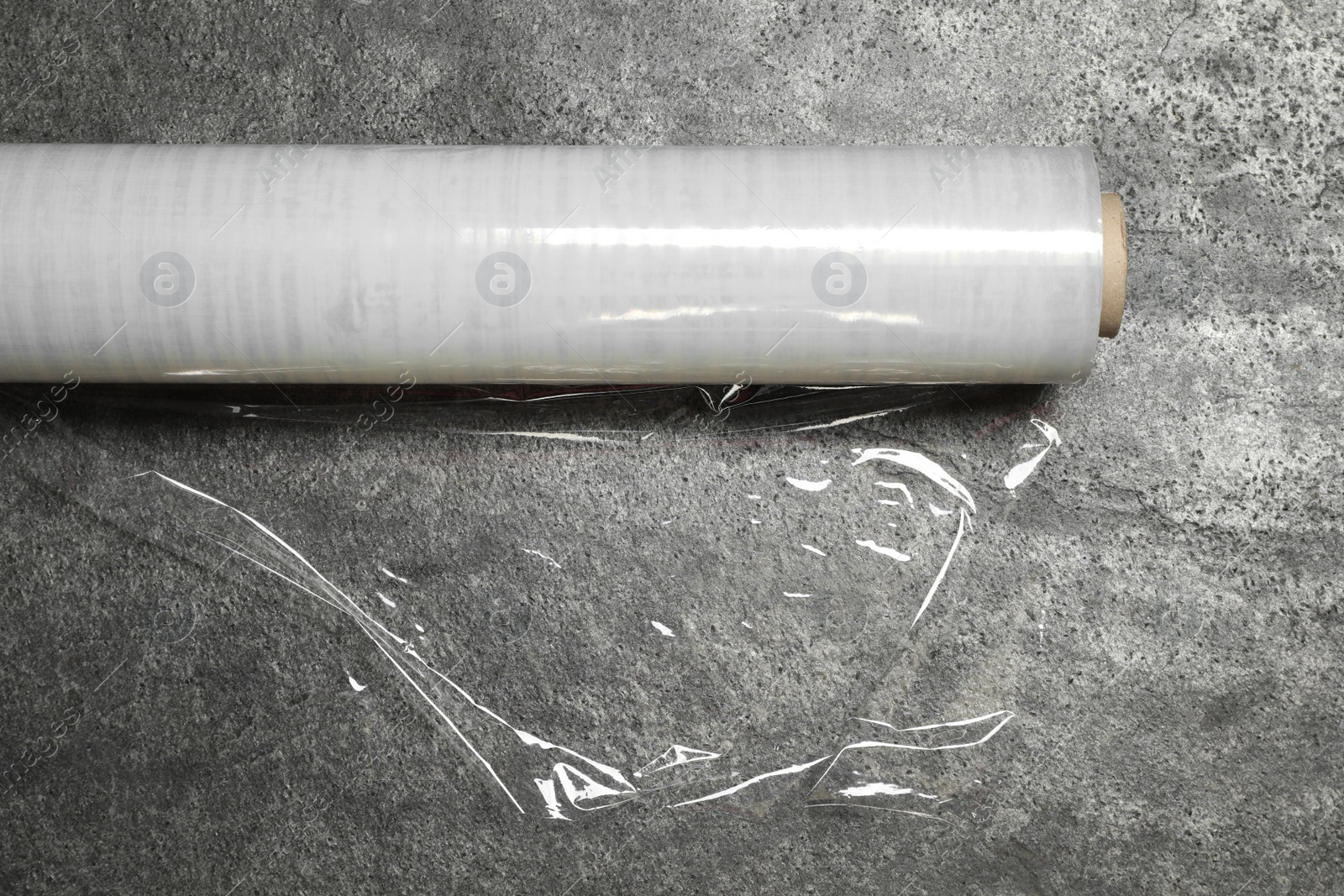 Photo of Roll of transparent plastic stretch wrap on grey table, closeup