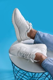 Man wearing stylish sneakers on white table against light blue background, closeup