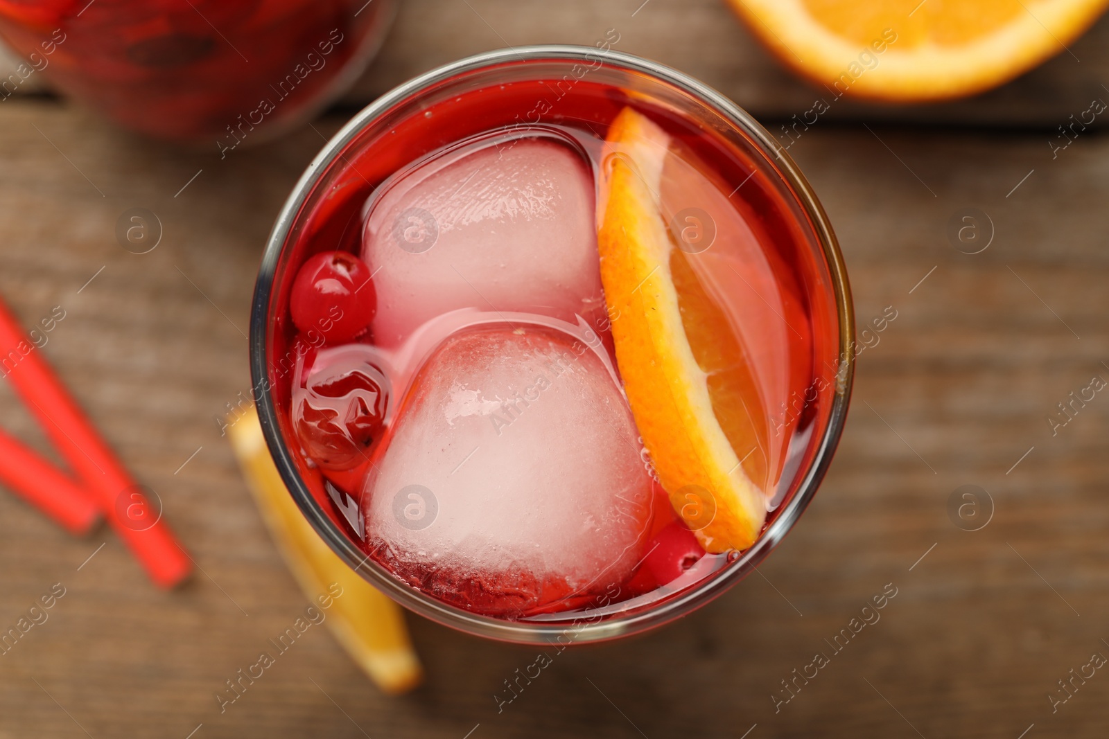 Photo of Tasty cranberry cocktail with ice cubes and orange in glass on wooden table, top view
