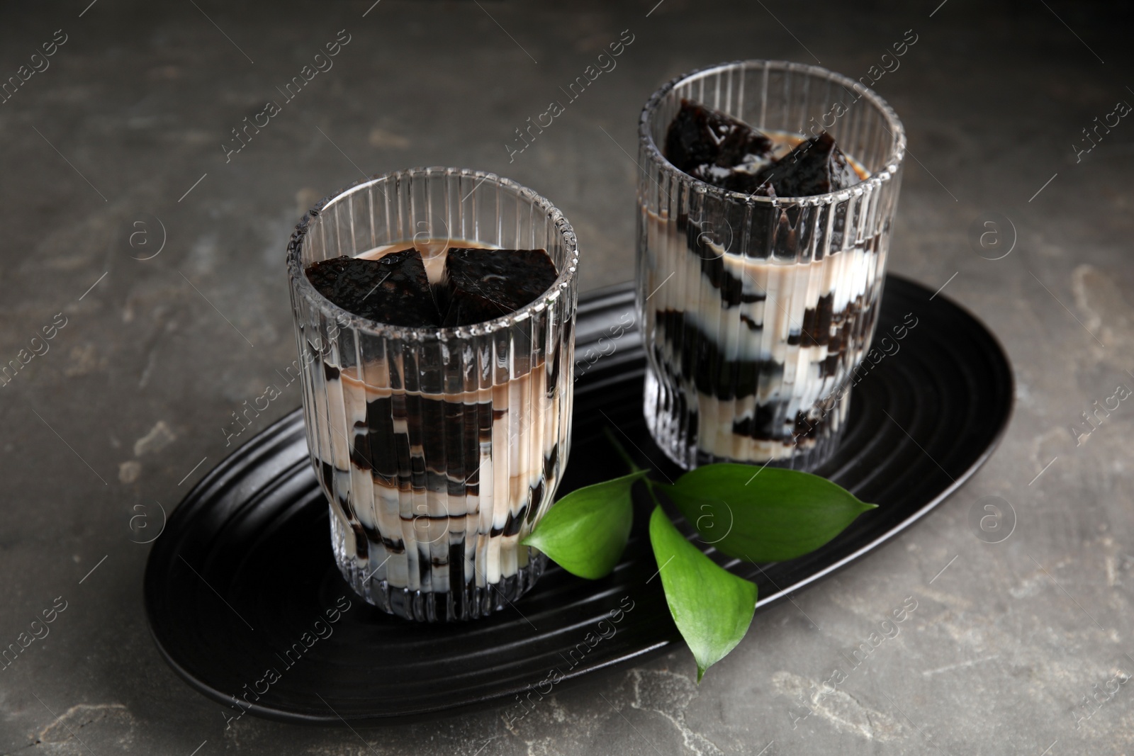 Photo of Glasses of milk with grass jelly and green leaves on grey table