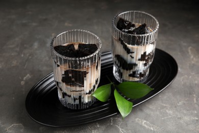 Photo of Glasses of milk with grass jelly and green leaves on grey table