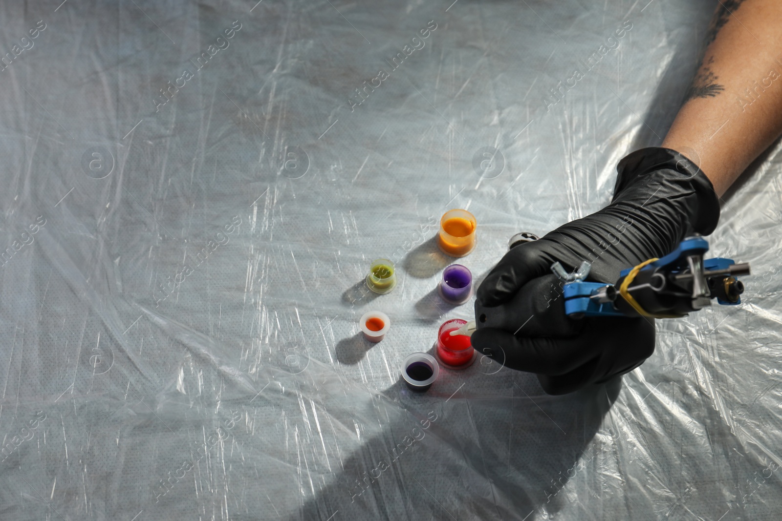 Photo of Tattoo artist with machine and inks at table, closeup. Space for text