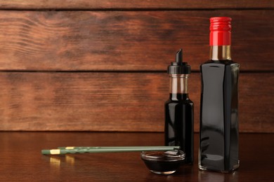 Bottles, bowl with soy sauce and chopsticks on wooden table. Space for text