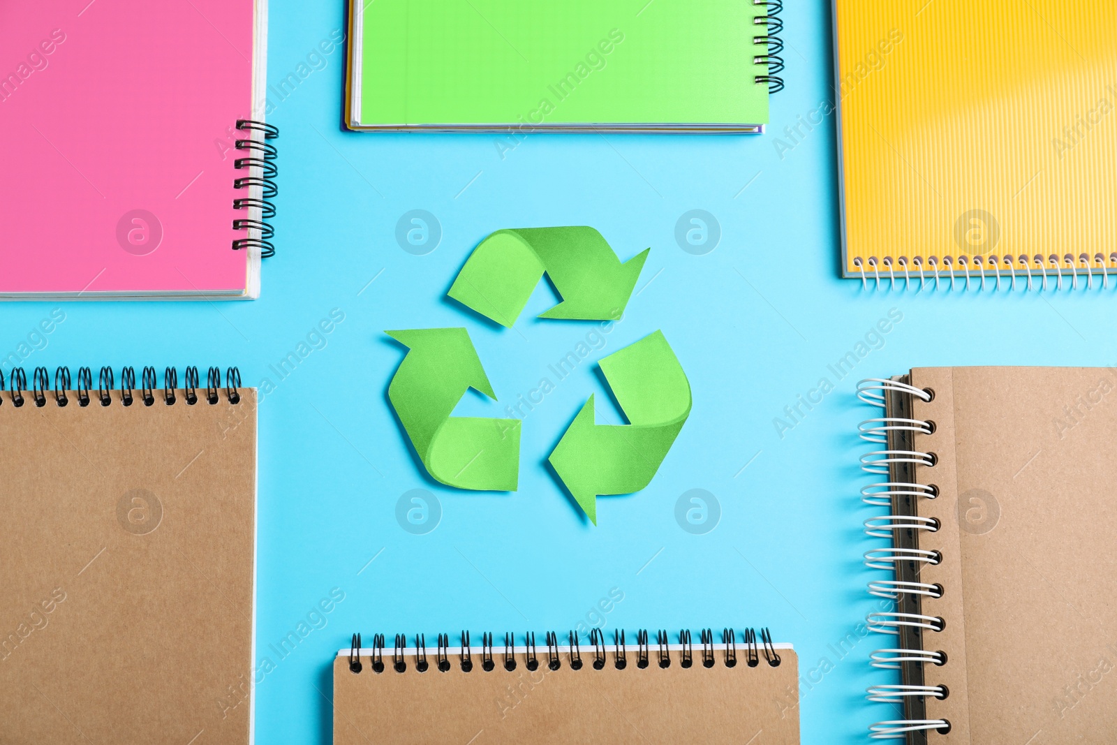 Photo of Recycling symbol, plastic and paper notebooks on light blue background, flat lay