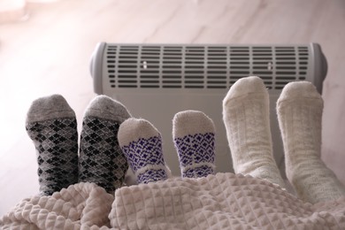 Photo of Family warming feet near electric heater at home, closeup