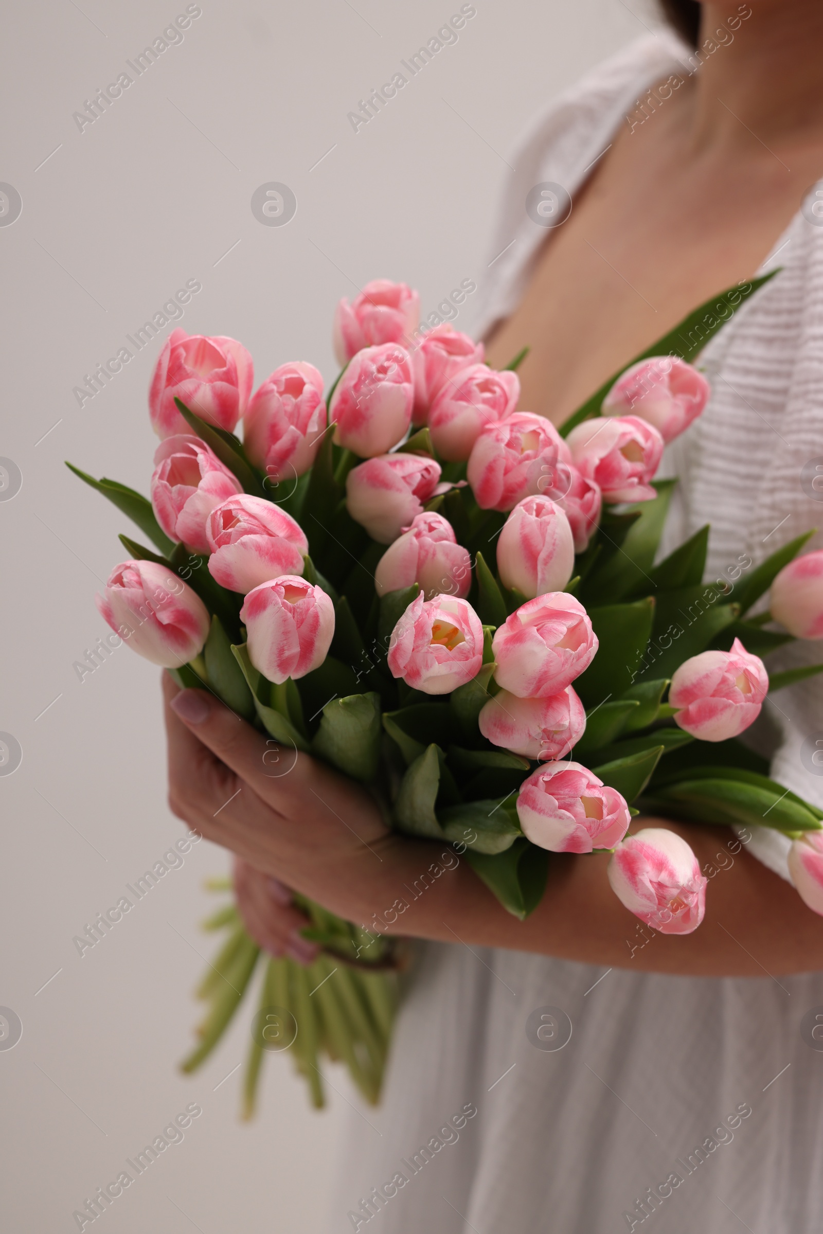 Photo of Woman with bouquet of beautiful fresh tulips on light grey background, closeup