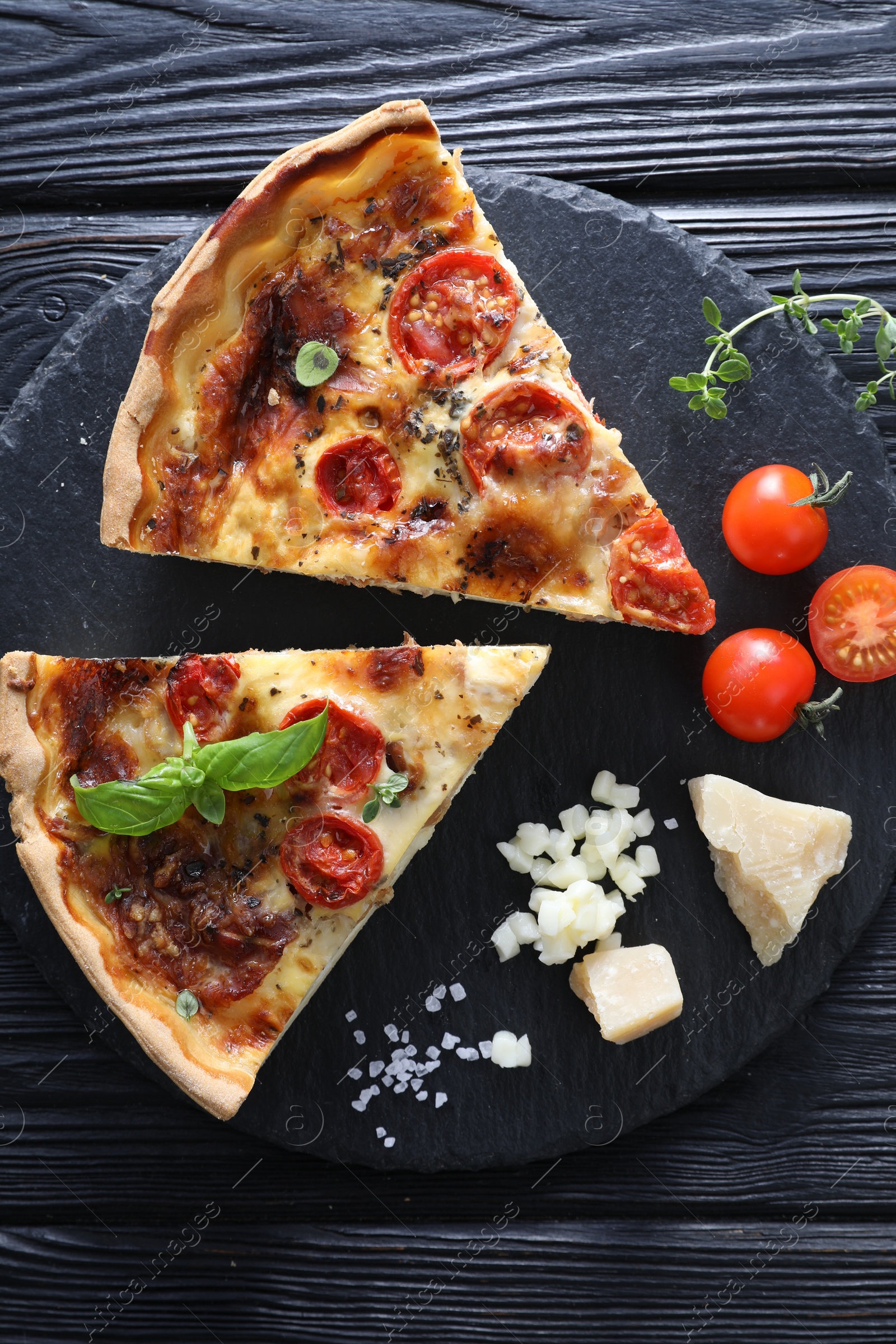 Photo of Pieces of delicious homemade quiche with prosciutto and ingredients on black wooden table, flat lay