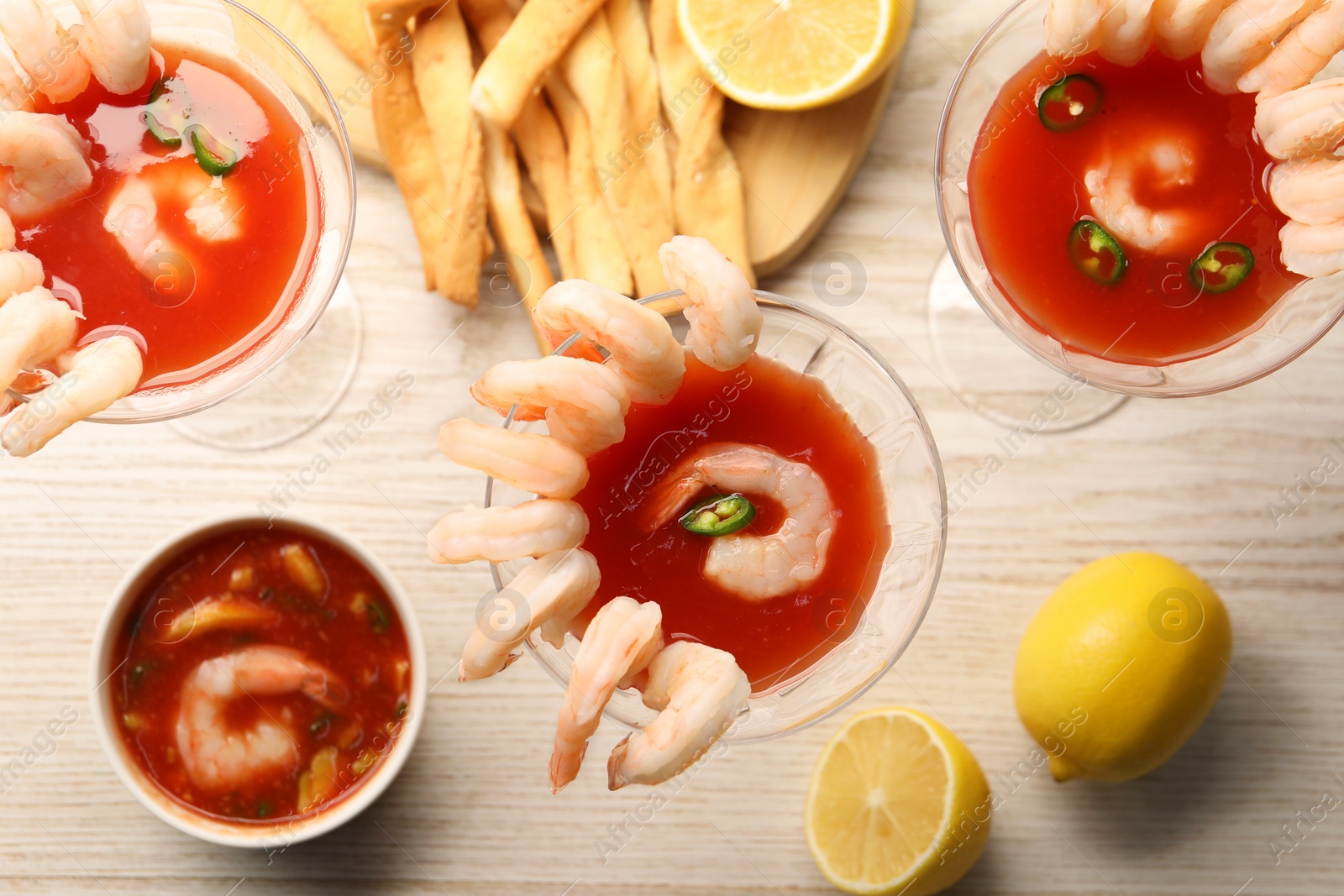 Photo of Tasty shrimp cocktail with sauce in glasses and lemon on light wooden table, flat lay