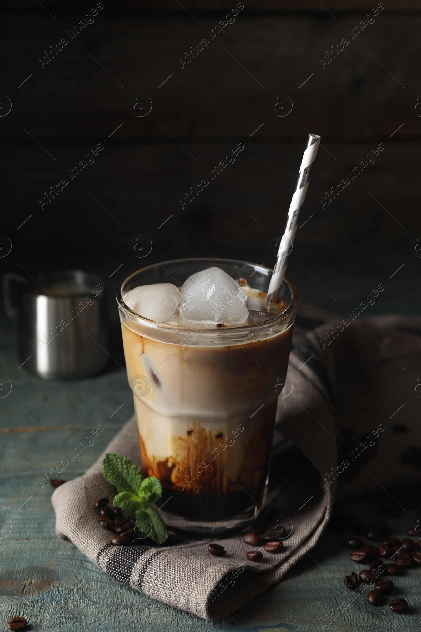 Photo of Glass of delicious iced coffee with milk, beans and mint on light blue wooden table