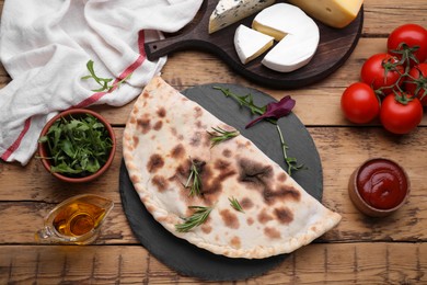 Delicious calzone and products on wooden table, flat lay