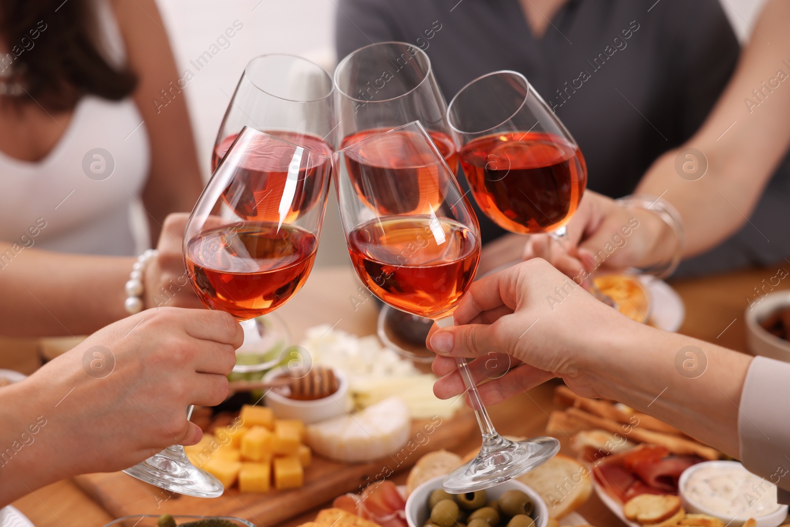 Photo of People clinking glasses with rose wine above wooden table indoors, closeup