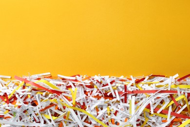 Shredded colorful paper strips on orange background, flat lay. Space for text