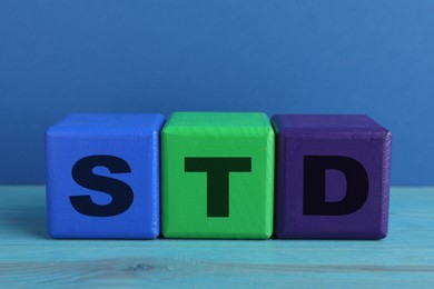 Photo of Abbreviation STD made with cubes on light blue wooden table