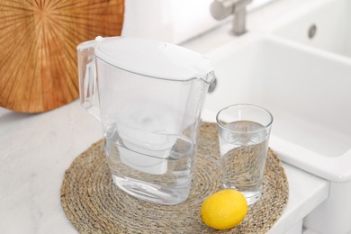 Photo of Water filter jug, glass and lemon on countertop in kitchen