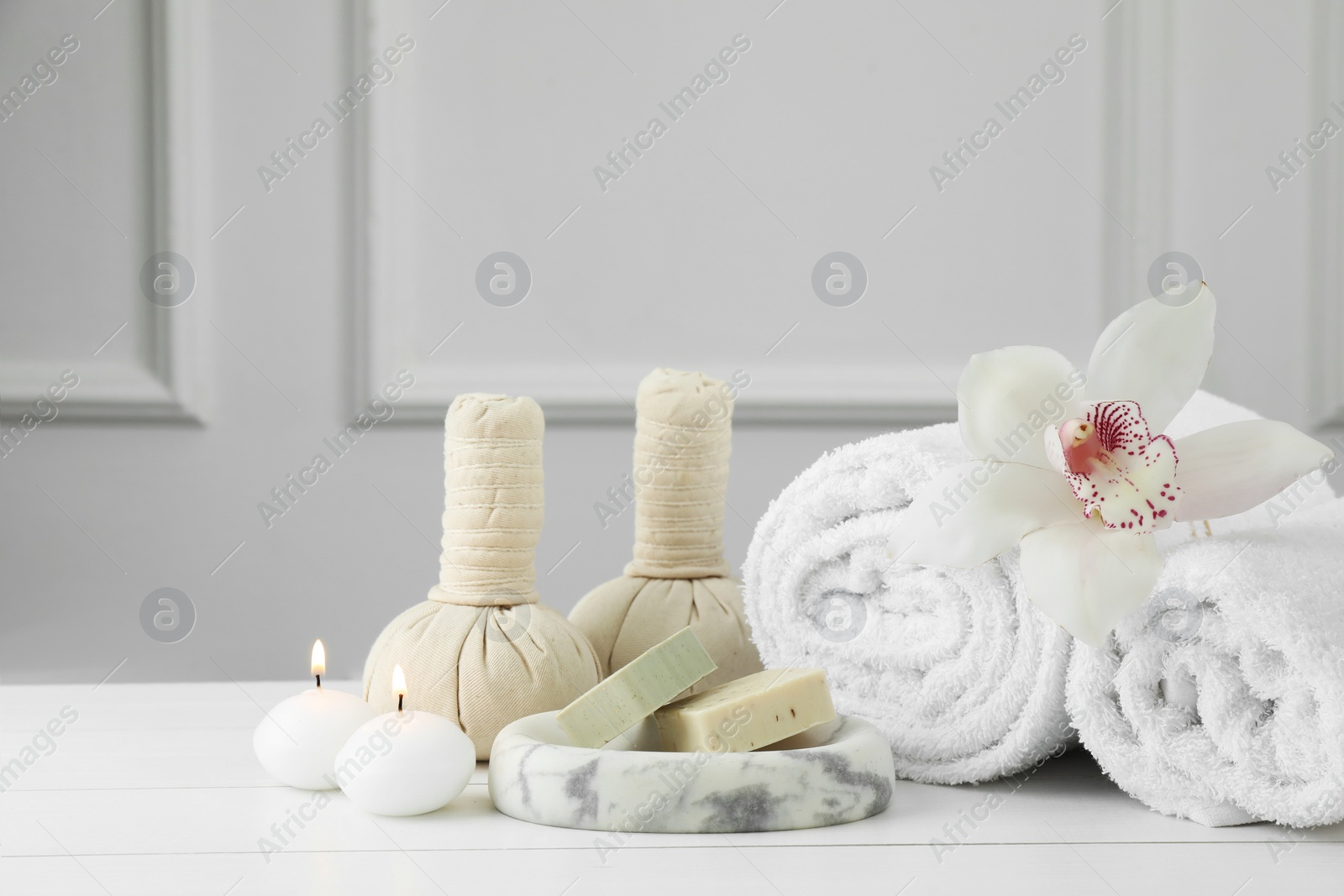 Photo of Beautiful spa composition. Towels, herbal bags, soap bars and burning candles on white wooden table, space for text