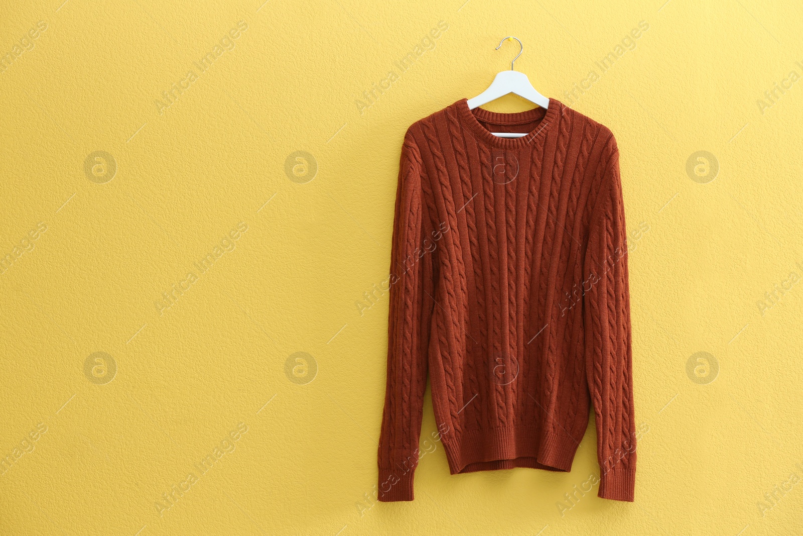 Photo of Hanger with stylish sweater on yellow wall. Space for text