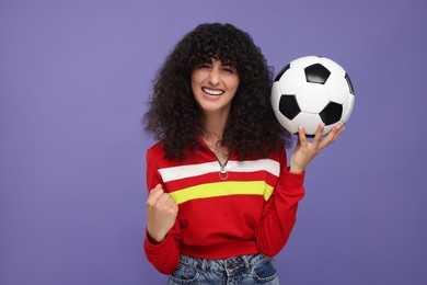 Photo of Happy fan holding soccer ball and celebrating on violet background