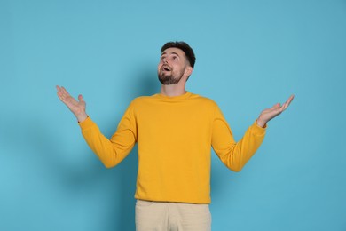 Surprised man in yellow sweatshirt on light blue background