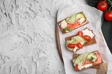 Photo of Tasty rye crispbreads with salmon, cream cheese and vegetables on grey textured table, flat lay. Space for text