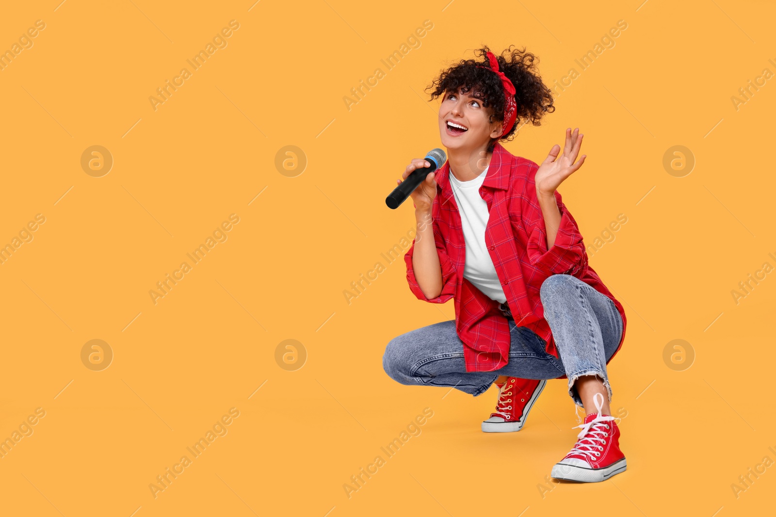 Photo of Beautiful young woman with microphone singing on yellow background. Space for text