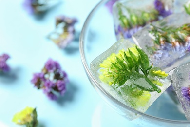 Photo of Bowl of ice cubes with flowers on blue background, closeup. Space for text
