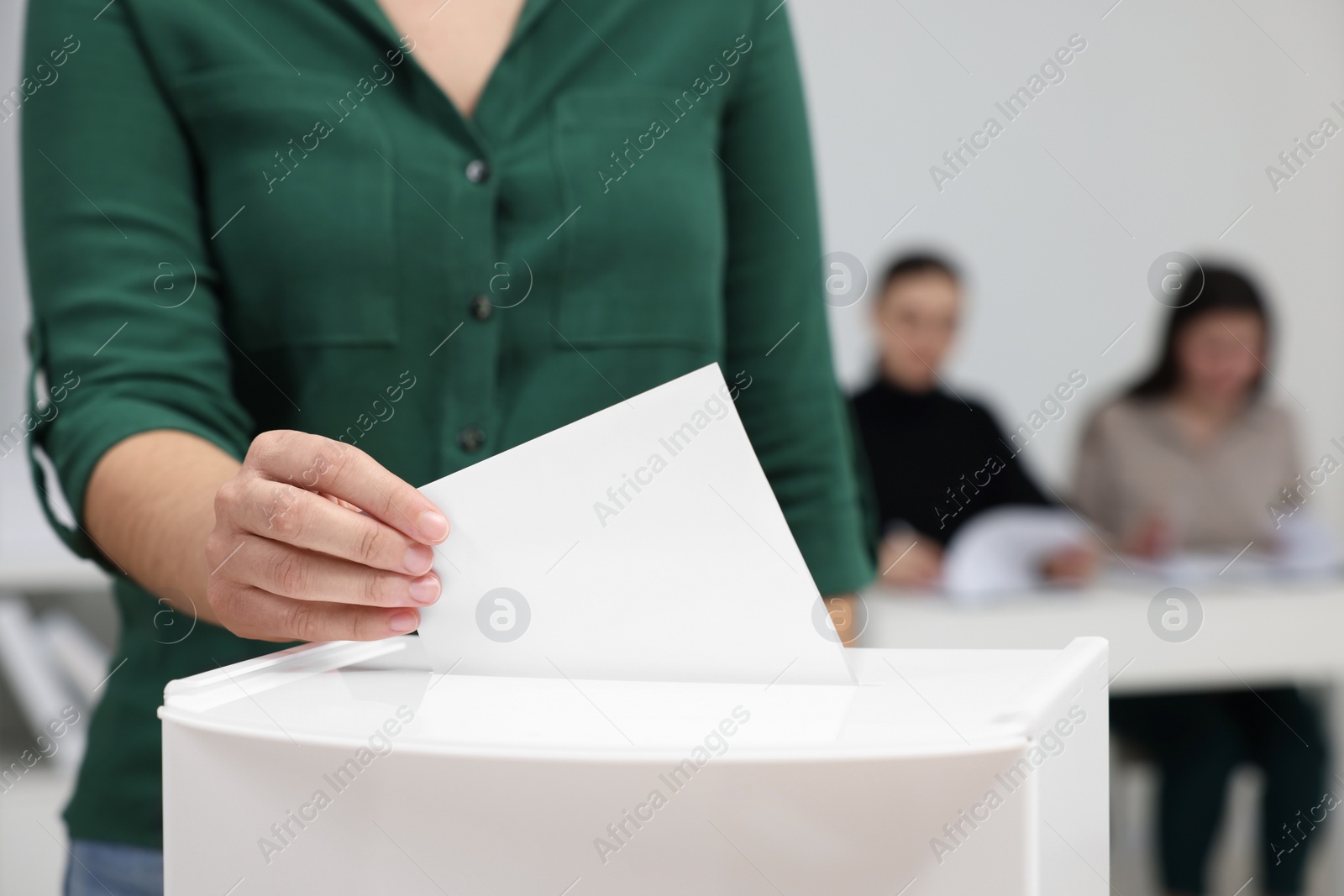 Photo of Woman putting her vote into ballot box on blurred background, closeup