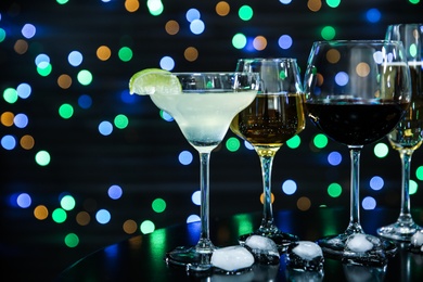 Photo of Many different alcoholic drinks on table against dark background with blurred lights