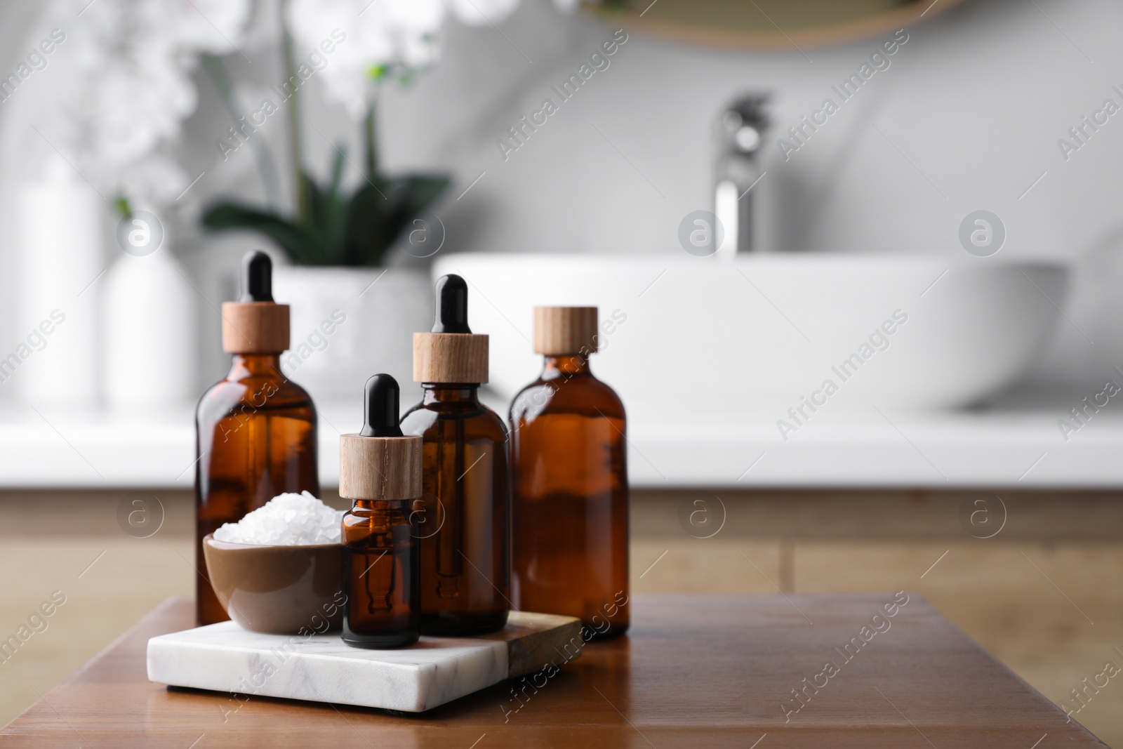 Photo of Essential oils and sea salt on wooden table in bathroom. Space for text