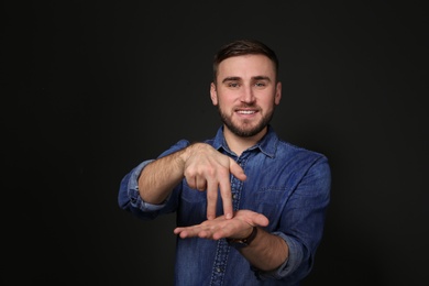 Photo of Man showing STAND gesture in sign language on black background