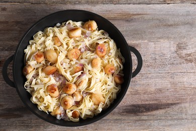 Delicious scallop pasta with onion in pan on wooden table, top view