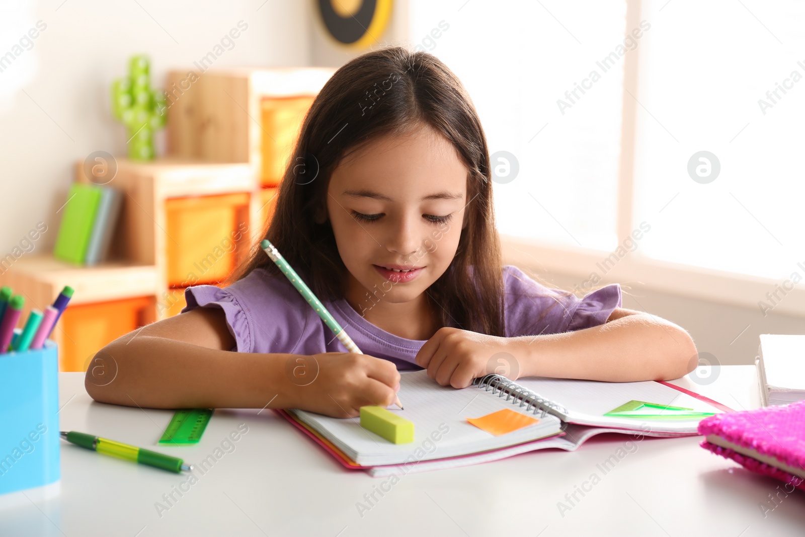 Photo of Little girl doing homework at table indoors