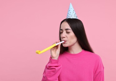 Woman in party hat with blower on pink background