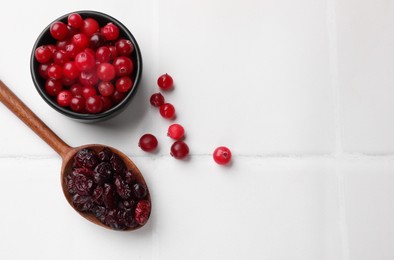 Tasty dried cranberries in spoon and fresh ones on white tiled table, top view. Space for text