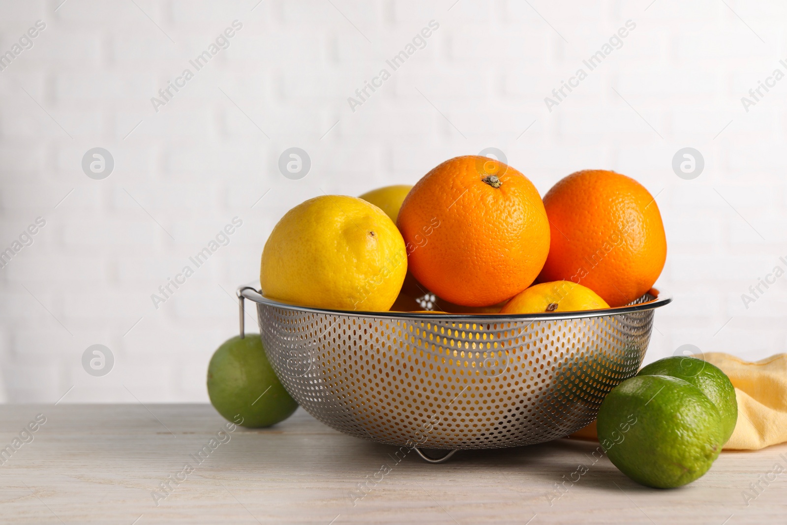 Photo of Different fresh fruits in colander on white wooden table. Space for text