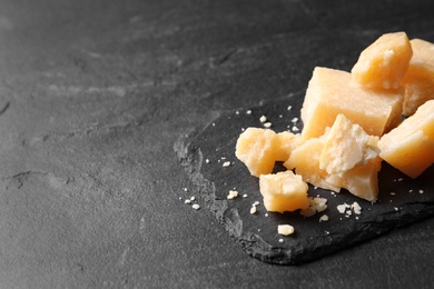 Photo of Pieces of delicious parmesan cheese on black table, closeup. Space for text