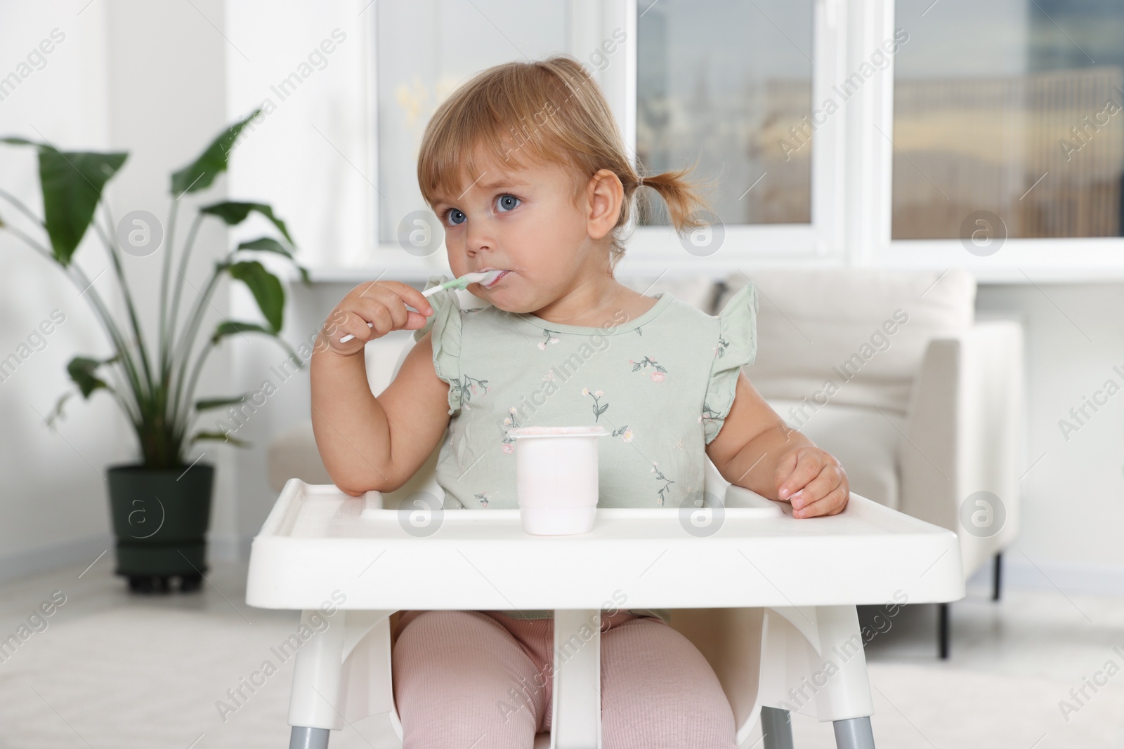 Photo of Cute little child eating tasty yogurt with spoon at home