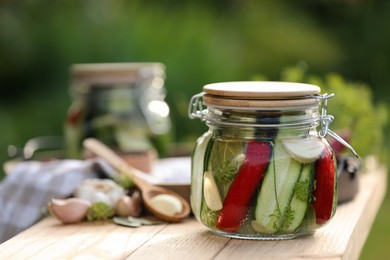 Photo of Jar of delicious pickled cucumbers and ingredients on wooden table against blurred background, closeup. Space for text