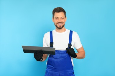 Professional worker with putty knife on light blue background