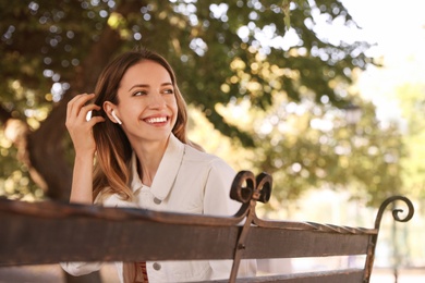 Young woman with wireless headphones listening to music in park. Space for text