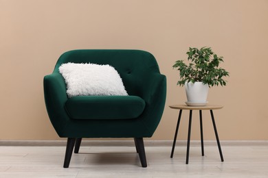 Photo of Stylish armchair and side table with plant near beige wall indoors