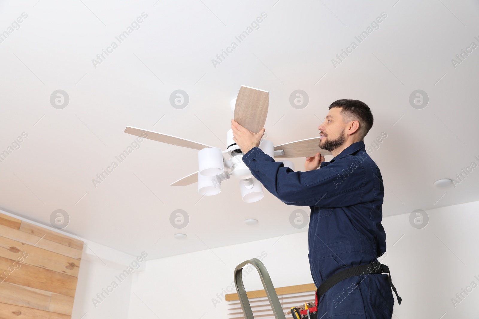 Photo of Electrician repairing ceiling fan indoors. Space for text