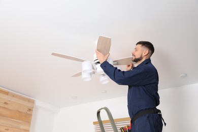 Photo of Electrician repairing ceiling fan indoors. Space for text