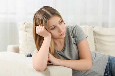 Upset teenage sitting alone on sofa at home