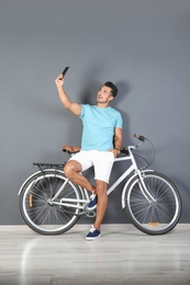 Photo of Handsome young hipster man taking selfie with bicycle near color wall